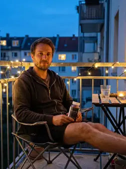 Mann auf dem Balkon mit Lichterkette am Abend